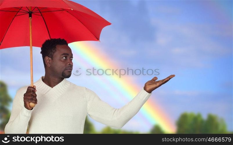 Attractive african man with a red umbrella and a beautiful rainbow