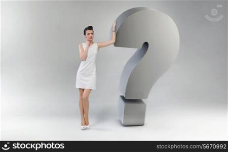 Attractive and astonished woman leaning against the huge question mark
