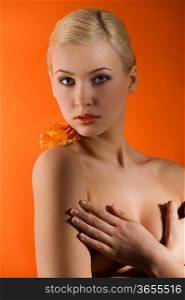 attractive and sensual young girl with stunning eyes and an orange rose on her naked shoulder on colored background