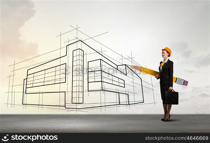 Attractive architect designer. Young female engineer in hard hat with big pencil and sketches at background