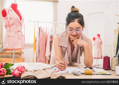 Attractive Asian female fashion designer working in home office workshop. Stylish fashionista woman creating new cloth design collection. Tailor and sewing. People lifestyle and occupation concept