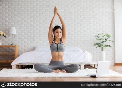 Attractive Asian woman looking laptop practice yoga lotus pose online course at home to meditation comfortable and relax,Health care and Exercise at home Concept,Self-isolation due COVID-19 pandemic