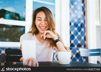Attractive beautiful happy young Asian woman taking a selfie usi. Attractive beautiful happy young Asian woman taking a selfie using a smart phone at cafe. Young Asian girl at restaurant taking self portrait.