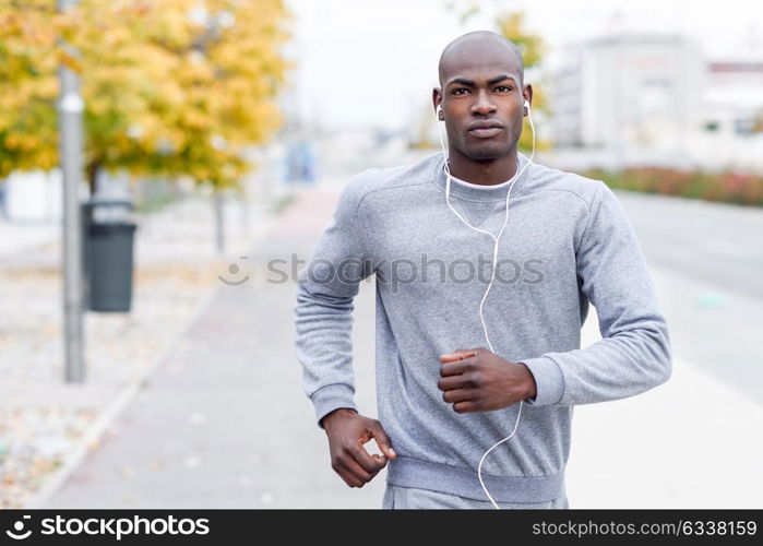 Attractive black man running in urban background. Male doing workout outdoors. Guy listening to music with white headphones