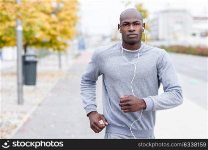 Attractive black man running in urban background. Male doing workout outdoors. Guy listening to music with white headphones