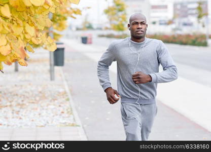 Attractive black man running in urban background. Male doing workout outdoors. Guy listening to music with white headphones