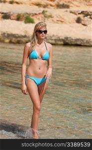 Attractive blond woman by the sea on the beach in bikini on sunny day