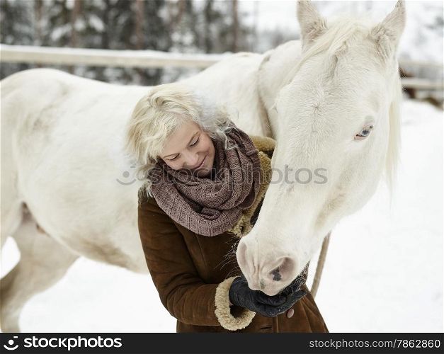 Attractive blond woman feeds a white horse, overcast winter day
