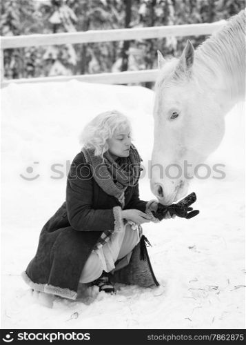 Attractive blond woman feeds a white horse, overcast winter day, black and white image