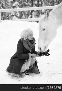 Attractive blond woman feeds a white horse, overcast winter day, black and white image