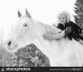 Attractive blond woman hugs a white horse, overcast winter day
