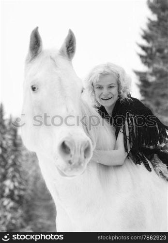 Attractive blond woman hugs a white horse, overcast winter day