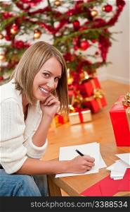 Attractive blond woman writing Christmas cards in front of tree