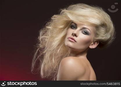 attractive blonde girl with fashion bushy creative hair-style posing with naked shoulders and cute make-up on red background. Looking in camera with charming expression