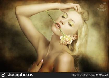 attractive blonde girl with long hair, colorful make-up and naked shoulders in fashion pose with flower between her lips