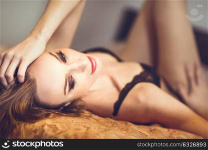 Attractive blonde woman in black lingerie posing on her bed. Young girl wearing underwear with long hair. Nice make-up with black eyeshadow and red lips.