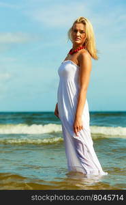 Attractive blonde woman on the beach.. Holidays beach summer and blonde lady. Attractive woman spending free time on the beach. Female wearing white dress and red necklace.