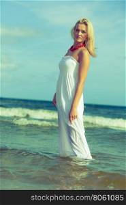 Attractive blonde woman on the beach.. Holidays beach summer and blonde lady. Attractive woman spending free time on the beach. Female wearing white dress and red necklace.