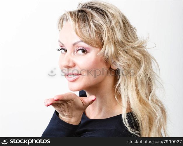 Attractive blonde woman portrait. Portrait of middle aged blonde woman. Adult female wearing dark blouse blowing kiss in studio.