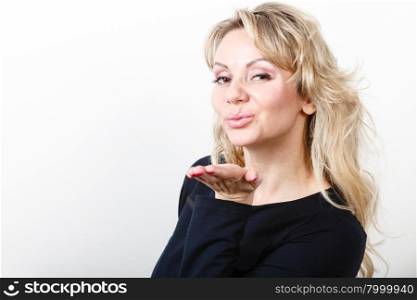 Attractive blonde woman portrait. Portrait of middle aged blonde woman. Adult female wearing dark blouse blowing kiss in studio.