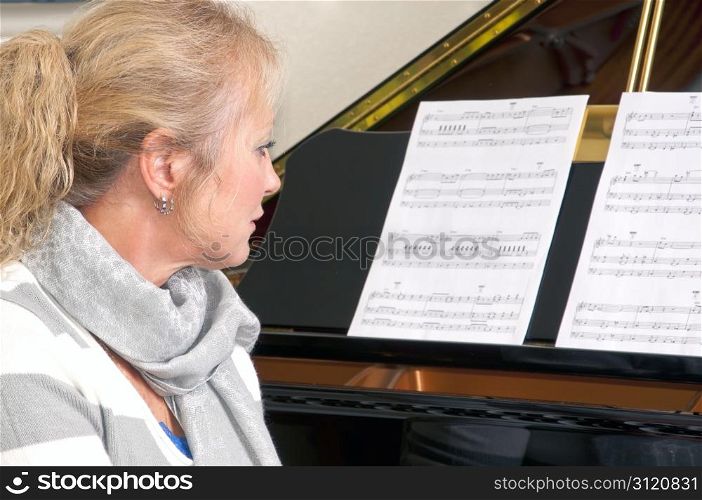 Attractive blonde woman sitting at a grand piano looking at sheet music.