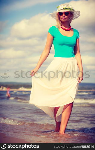 Attractive blonde woman wearing long romantic dress walking on beach and relaxing during summer.. Blonde woman wearing dress walking on beach