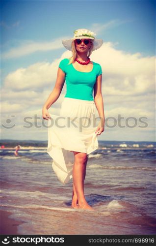 Attractive blonde woman wearing long romantic dress walking on beach and relaxing during summer.. Blonde woman wearing dress walking on beach