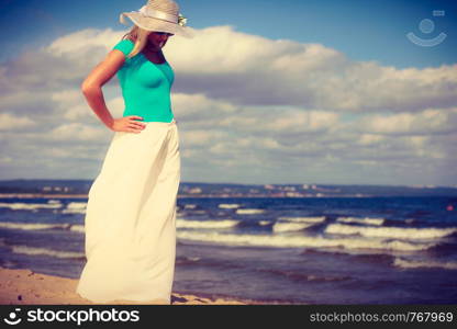 Attractive blonde woman wearing long romantic dress walking on beach and relaxing during summer.. Blonde woman wearing dress walking on beach