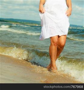 Attractive blonde woman wearing long white romantic dress walking in water sea during summer.. Blonde woman wearing dress walking in water