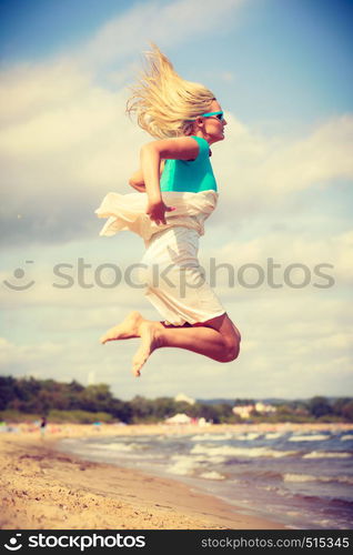 Attractive blonde woman wearing romantic dress jumping on beach and relaxing during summer.. Blonde woman wearing dress playing jumping on beach