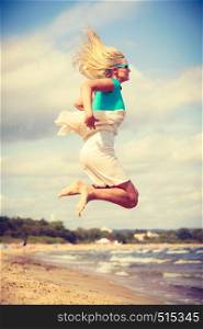Attractive blonde woman wearing romantic dress jumping on beach and relaxing during summer.. Blonde woman wearing dress playing jumping on beach