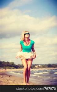 Attractive blonde woman wearing romantic dress walking on beach and relaxing during summer.. Blonde woman wearing dress walking on beach