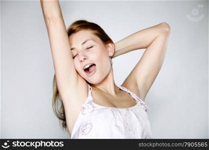 Attractive blonde woman with no make up yawning and stretching gray background