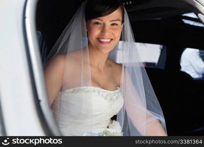 Attractive bride sitting in car and smiling