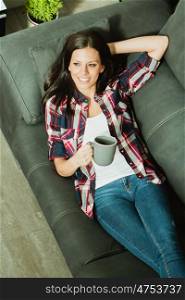 Attractive brunette girl resting on the sofa and drinking a cofee