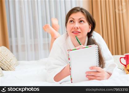 Attractive brunette with a notebook and pen on the bed