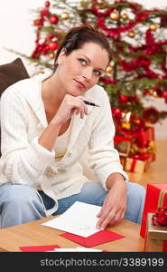 Attractive brunette writing Christmas cards in front of tree