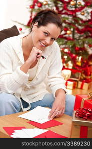 Attractive brunette writing Christmas cards in front of tree