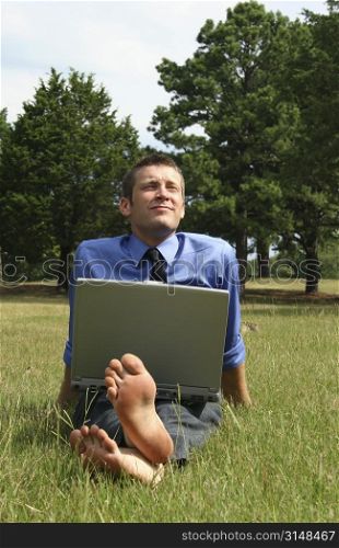 Attractive business man barefoot in the grass with laptop.