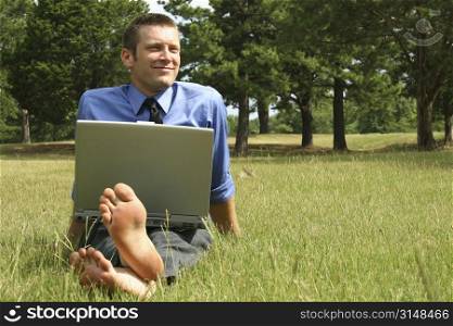 Attractive business man barefoot with laptop in grass.