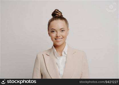 Attractive business woman, happy after conference, in beige suit, white shirt, hair bun, smiling at camera on grey background. 