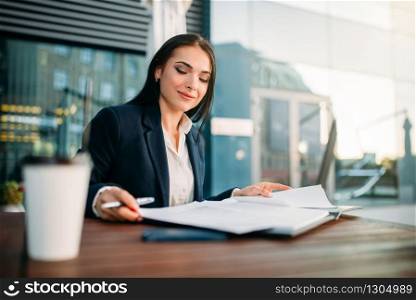 Attractive business woman works at lunch in cafe. Modern building, financial center, cityscape. Female businessperson in suit at workplace. Attractive business woman works at lunch in cafe