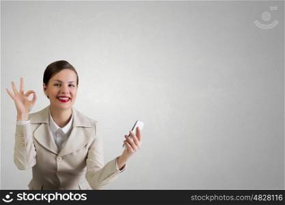 Attractive businesswoman having mobile conversation. Young pretty businesswoman sitting at table with mobile phone in hand showing ok gesture