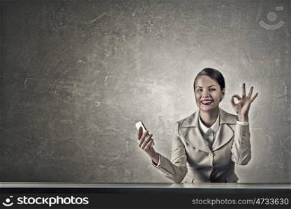 Attractive businesswoman in grunge style. Beautiful businesswoman with phone in hand sitting at table and showing ok gesture