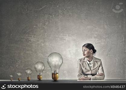 Attractive businesswoman sitting at table. Young businesswoman sitting at table and looking away on light bulbs