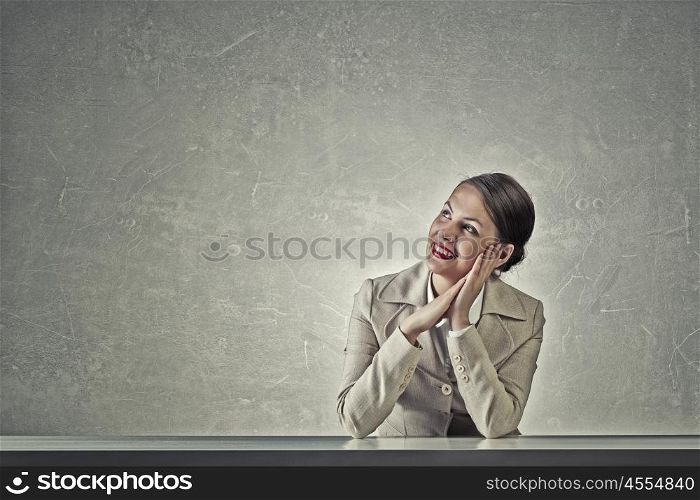 Attractive businesswoman sitting at table. Young businesswoman sitting at table and looking dreamily away
