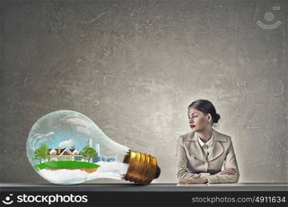 Attractive businesswoman sitting at table. Young businesswoman sitting at table and looking dreamily away. Ecology concept