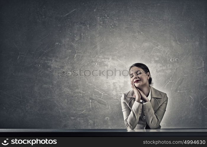 Attractive businesswoman sitting at table. Young businesswoman sitting at table and looking dreamily away