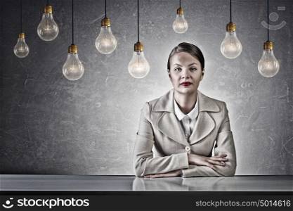 Attractive businesswoman sitting at table. Young businesswoman sitting at table in concrete grunge styled room and bulbs hanging from above