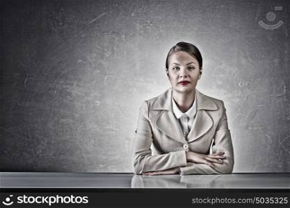 Attractive businesswoman sitting at table. Young businesswoman sitting at table in concrete grunge styled room